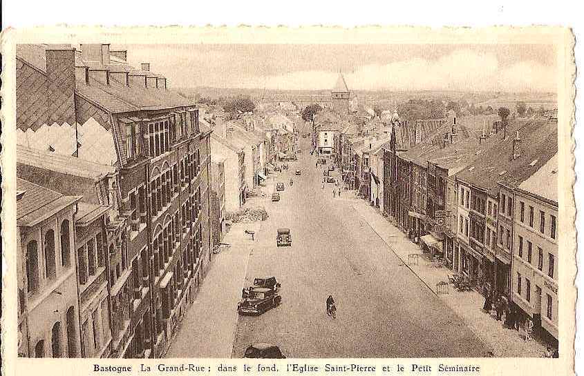 BASTOGNE LA GRANDE RUE DANS LE FOND L'EGLISE SAINT PIERRE ET LE PETIT SEMINAIRE (PERSONNAGES,AUTO) REF 18000 - Bastogne