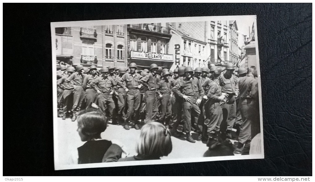 Une Photo De Militaires , En File, En Ville, Enseigne " Ro?lants". Cachet Au Dos: Un Nom( De Militaire?) , Ville Heusy. - Guerra, Militari