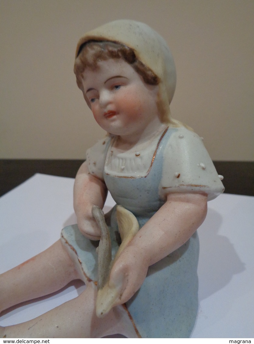 Muñeca de porcelana biscuit. Niña con gorro, sentada con unas tijeras.