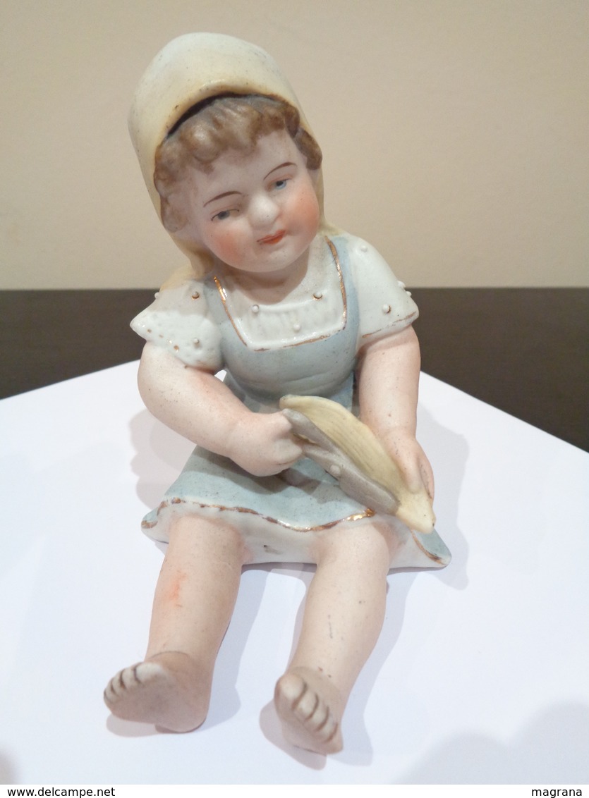 Muñeca de porcelana biscuit. Niña con gorro, sentada con unas tijeras.