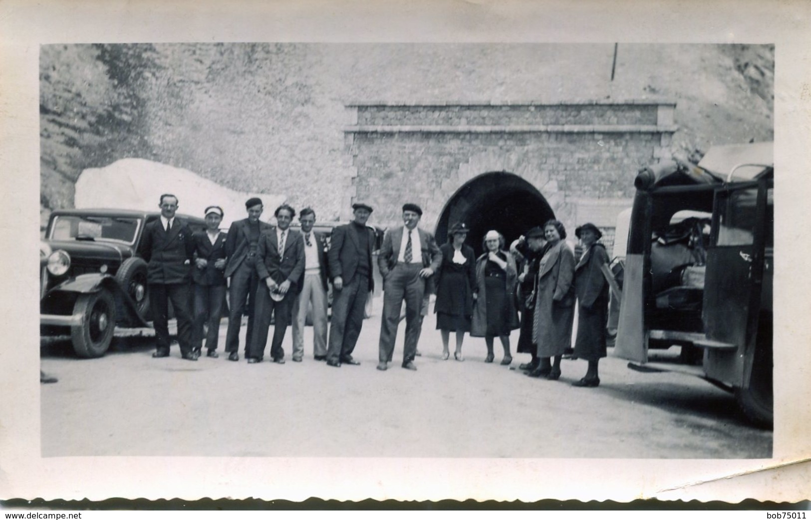 Photo D'hommes Et De Femmes Souriant Devant Un Tunnel Et D'unevieille Voiture Et L'arrière D'un Vieux Car Ouvert En 1939 - Automobiles