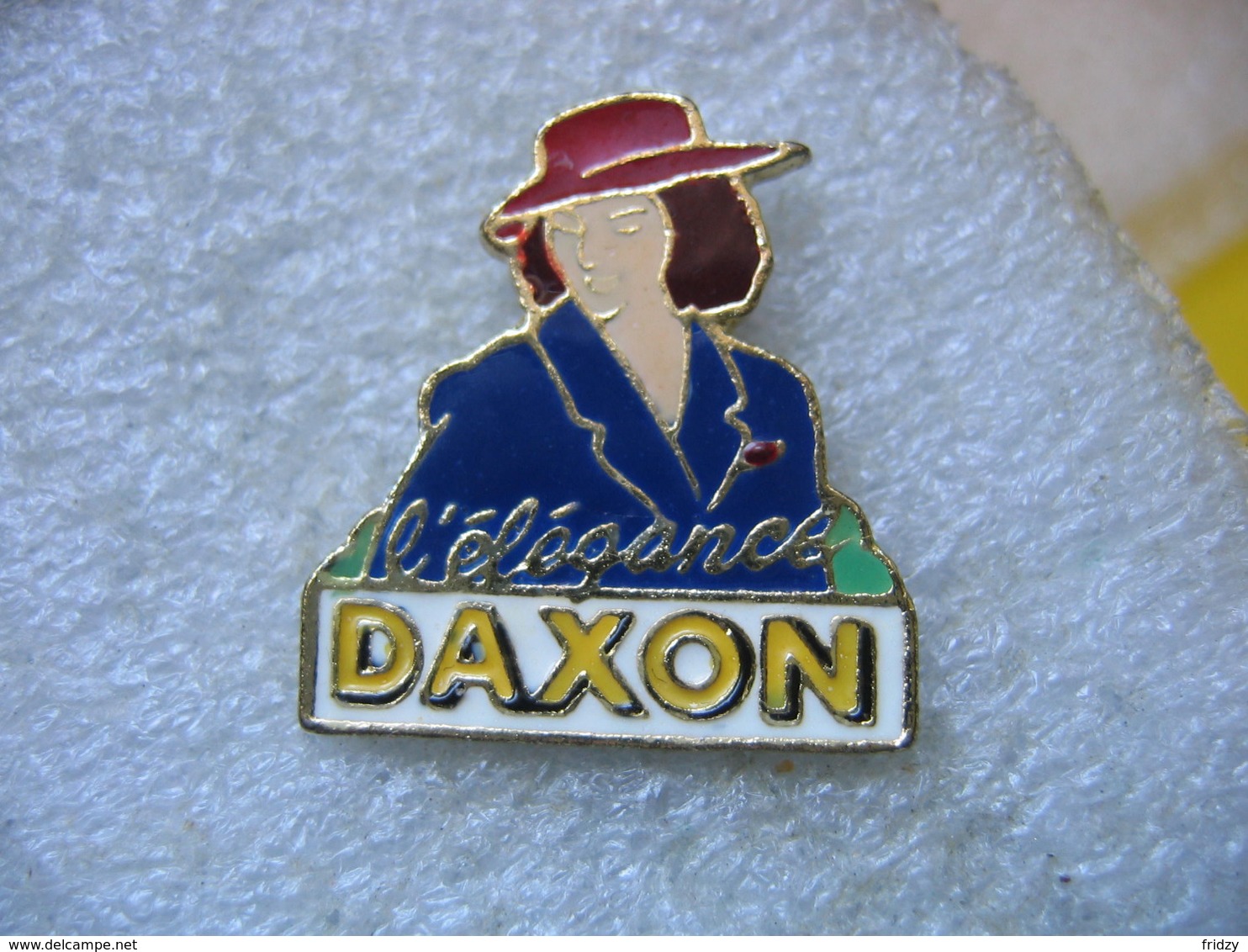 Pin's DAXON, L'élégance. Marque Française De Vente à Distance En Prêt-à-porter Femme Et Homme, Lingerie Et Chaussures - Autres & Non Classés