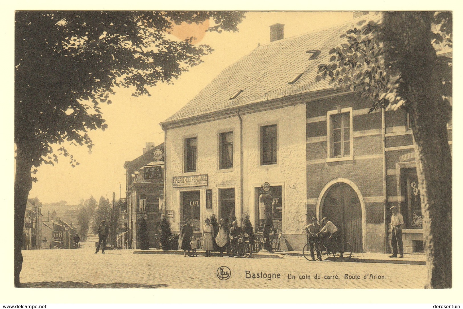 A0889	[Postkaart] Bastogne / Un Coin Du Carré. Route D’Arlon (Nels, Schumacher) [café Naftpomp Pierre Delperdange] - Bastenaken