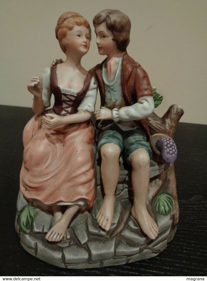 Figura de porcelana  biscuit pintada de una pareja galante sentada en un banco.