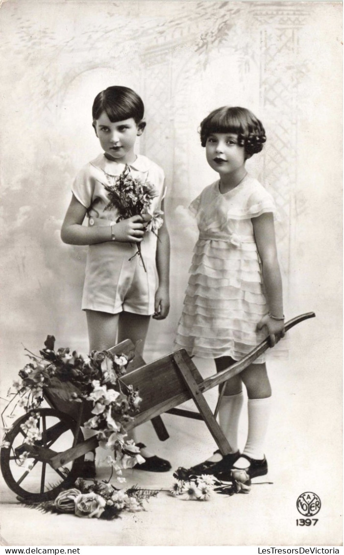 Enfants - Un Frère Et Une Sœur Posant Près D'une Brouette De Fleurs -  Carte Postale Ancienne - Groupes D'enfants & Familles