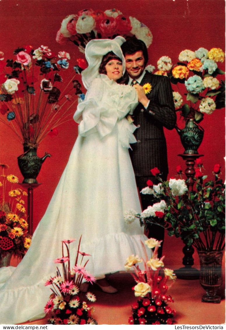 NOCES - L'époux Et La Mariée - Des Mariés Entourés De Fleurs - Murs Rouges - Colorisé - Carte Postale - Noces