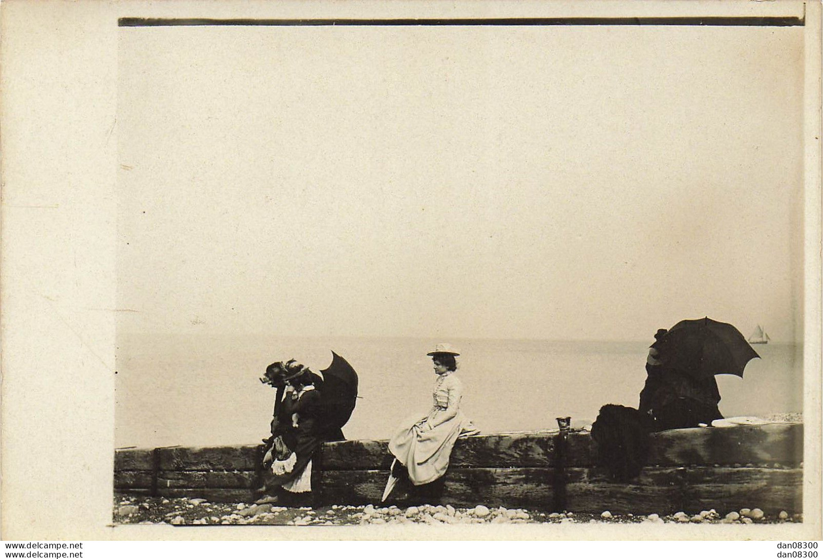 CARTE PHOTO NON IDENTIFIEE REPRESENTANT  UNE FEMME ASSISE SUR LE MURET D'UNE DIGUE DEVANT LA MER AU LOIN UN VOILIER - To Identify