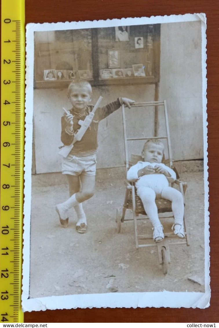 #11  - Enfant Child  Boy Garcon - With A Rifle. She Looks After A Baby In A Stroller In Front Of A Photography Shop - Anonyme Personen