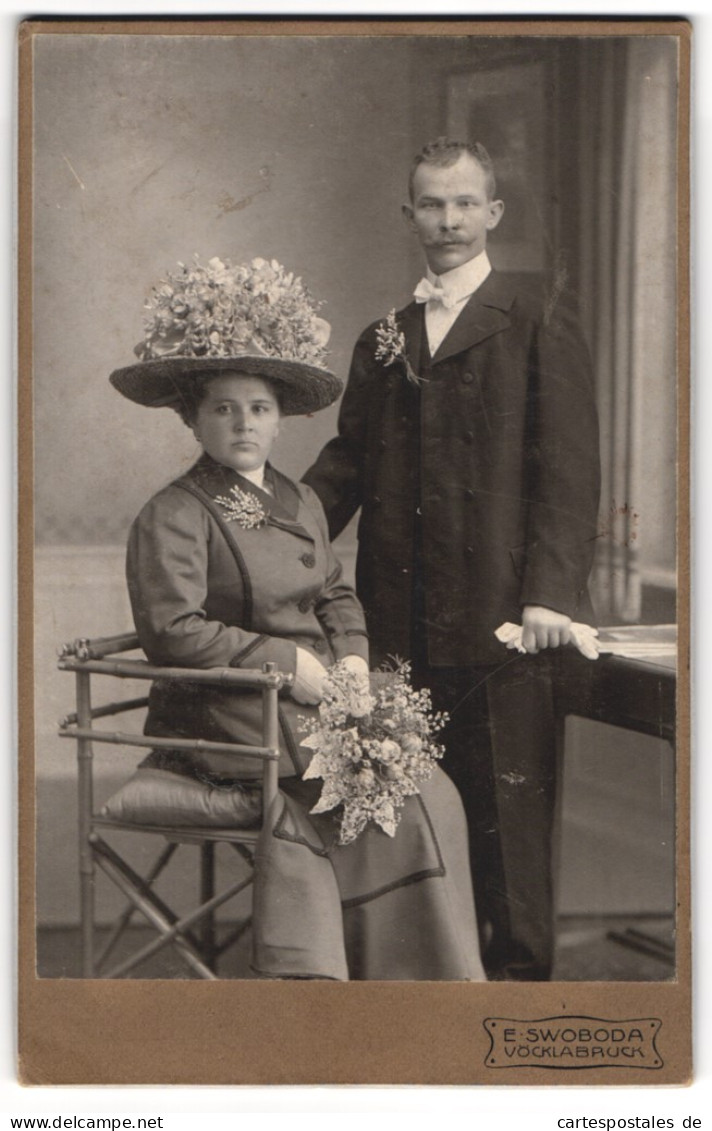 Fotografie E. Swoboda, Vöcklabruck, Ehepaar Im Dunklen Kleid Mit Blumenhut Und Mann Im Anzug  - Anonieme Personen