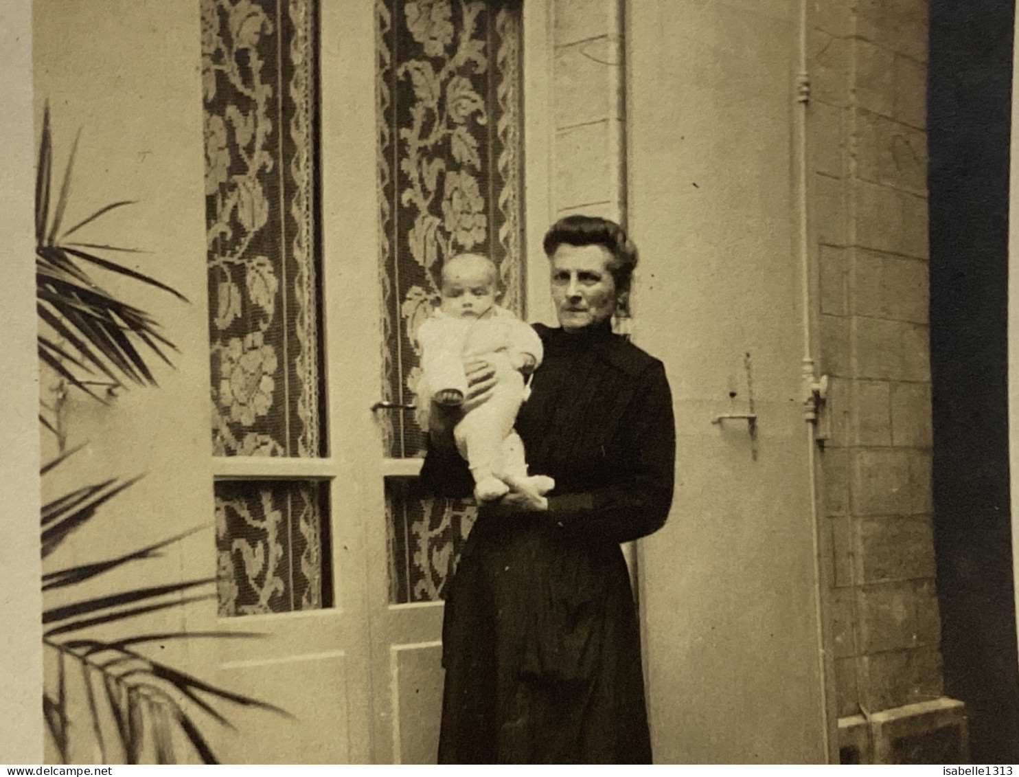 Photo Ancienne Snapshot 1930 Femme, Habillée En Noir Devant Ses Fenêtres, Volets Bébé Dans Les Bras Habillé En Blanc - Anonymous Persons