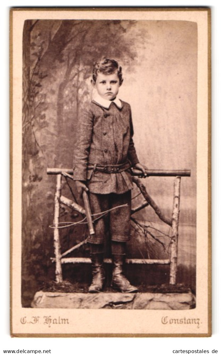 Fotografie C. F. Halm, Constanz, Rosgartenstr. 20, Portrait Frecher Bube Im Anzug Am Holzgeländer Stehend  - Anonieme Personen