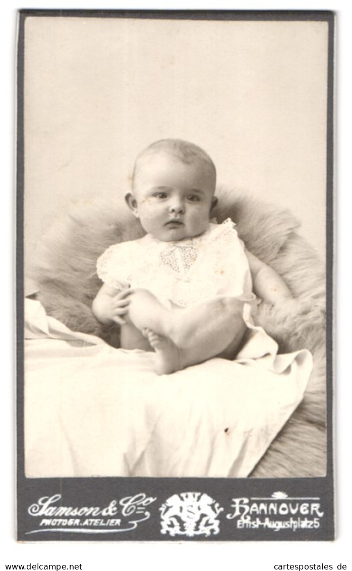 Fotografie Samson & Co., Hannover, Ernst-August-Platz 5, Portrait Süsses Baby Im Weissen Kleidchen Auf Fell Sitzend  - Anonyme Personen