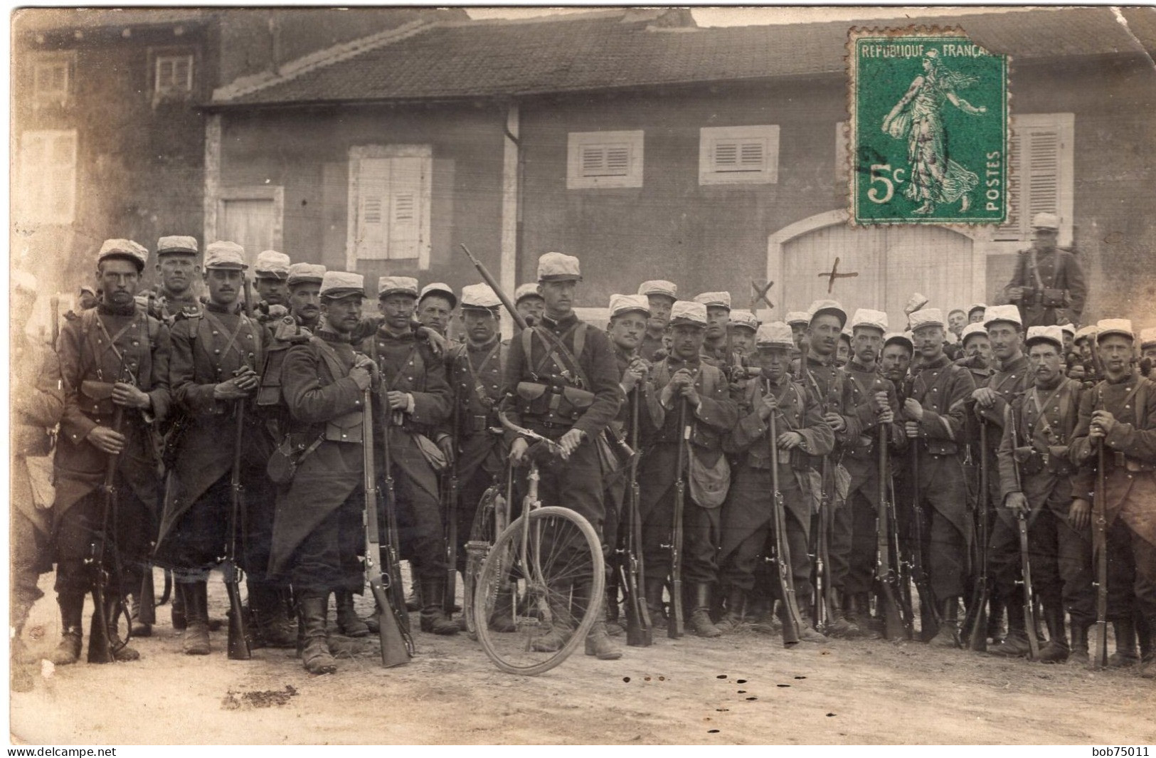 Carte Photo D'une Compagnie De Soldats Francais En Tenue De Combats Et Avec Leurs Fusil Et Un Vélo Dans Un Village - Guerra, Militares