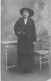 PHOTOGRAPHIE -FEMME - DEBOUT - TABLE - MANTEAU NOIR - JUPE NOIRE - CHAPEAU - GANTS NOIR - CARTE POSTALE ANCIENNE - Photographie