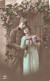 COUPLES - Un Couple Se Tenant Devant La Porte Décorée Par Des Fleurs  - Colorisé - Carte Postale Ancienne - Paare