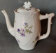 Cafetière En Porcelaine, Blanche Motif Floral Violet. Un Casse Sur Le Bec Verseur. - Other & Unclassified