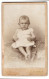 Fotografie R. Jarmer, Aachen, Friedrich-Wilhelm-Platz 5, Portrait Süsses Baby Im Weissen Kleidchen Auf Fell Sitzend  - Anonyme Personen