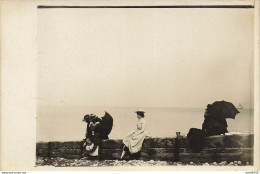 CARTE PHOTO NON IDENTIFIEE REPRESENTANT  UNE FEMME ASSISE SUR LE MURET D'UNE DIGUE DEVANT LA MER AU LOIN UN VOILIER - A Identifier