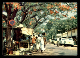 GUINEE - CONAKRY - RUE DE LA VILLE BORDEE DE FLAMBOYANTS ET D'ETALAGES EXOTIQUES - Guinée