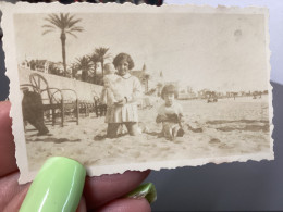 Photo Snapshot 1920 Cannes Petite Fille à Genoux Dans Le Sable à La Plage Poupon Dans Les Mains Fille, Assis Assise à Cô - Personnes Anonymes