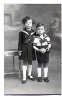 Carte Photo D'une Petite Fille élégante Avec Un Jeune Garcon Posant Dans Un Studio Photo Vers 1920 - Personnes Anonymes