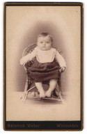 Fotografie Heinrich Weber, Winnenden, Portrait Niedliches Kleinkind Im Hübschen Kleid Mit Latz Auf Korbstuhl Sitzend  - Anonieme Personen
