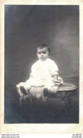 CARTE PHOTO NON IDENTIFIEE REPRESENTANT UN BEBE ASSIS SUR UNE TABLE DANS UN STUDIO PHOTO - Te Identificeren