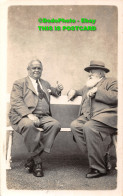 R359463 Two Men Are Sitting On A Bench. A Man With A Beard And A Hat And A Walki - World