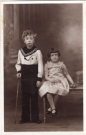 Carte Photo D'une Jeune Fille élégante Avec Un Jeune Garcon Posant Dans Un Studio Photo Vers 1930 - Personnes Anonymes