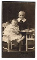 Fotografie Gebr. Schulze, Osnabrück, Grosse Str. 19, Portrait Niedlicher Kinderpaar Mit Buch Am Tisch Sitzend  - Personnes Anonymes