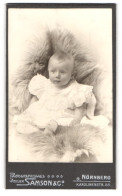 Fotografie Samson & Co., Nürnberg, Karolinenstrasse 55, Baby Im Weissen Kleidchen In Pelz Sitzend  - Anonieme Personen