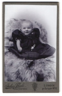 Fotografie Julius Thiele, Lübeck, Gr. Burgstr. 15, Lächelndes Kleinkind In Zu Grossem Kleid Auf Fell  - Personnes Anonymes