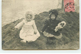 Enfant - Fillettes Assise Dans Le Sable, Une Tenant Une Poupée - Portraits