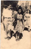 Carte Photo D'une Jeune Femme élégante Avec Un Jeune Homme Se Promenant Dans Les Rue D'une Ville - Personnes Anonymes