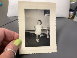 Photo Snapshot Noir Et Blanc, 1960 Petit Bébé, Garçon Fille, En Blanc, Debout Devant Sa Chaise Haute - Anonymous Persons